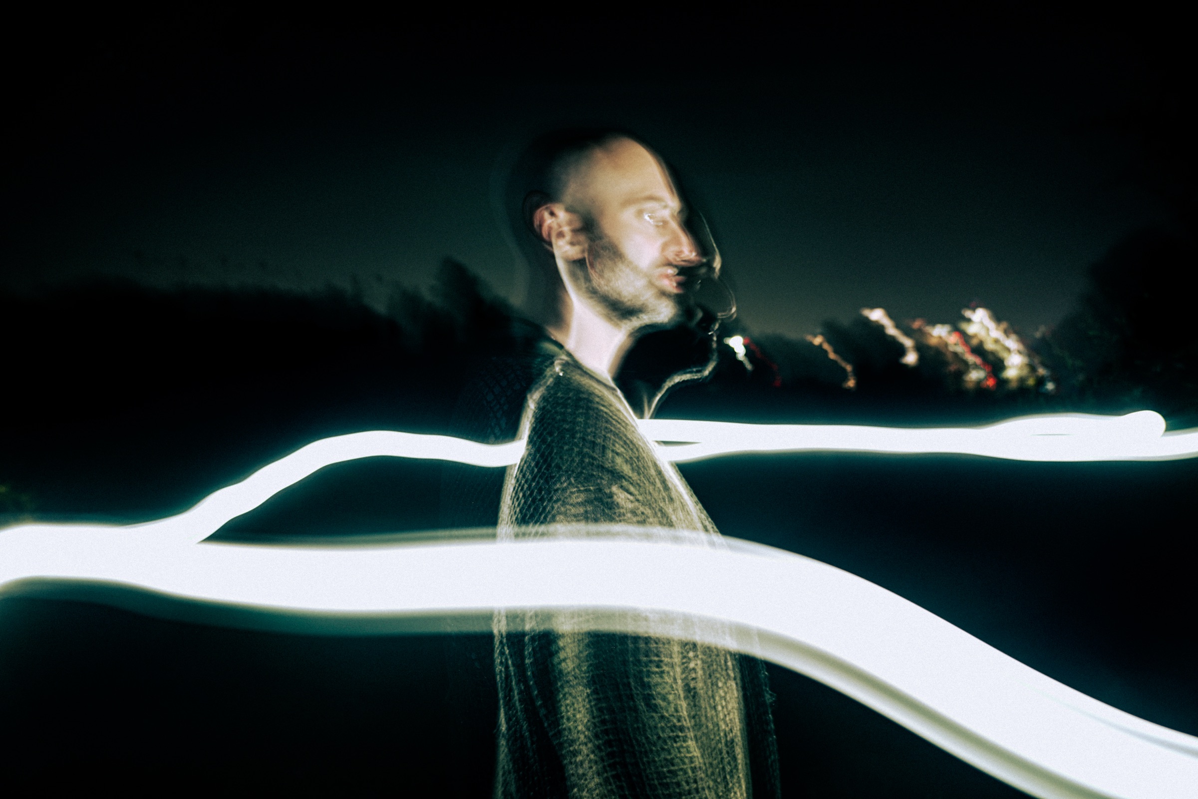 DECAP in profile at night, two long ribbons of light painted across him by a slow shutter.